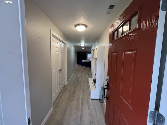 hall with light hardwood / wood-style flooring and a textured ceiling