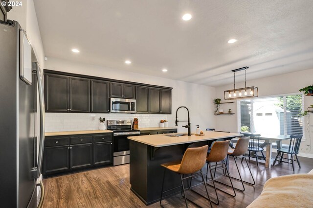 kitchen with appliances with stainless steel finishes, a breakfast bar, decorative light fixtures, sink, and a kitchen island with sink