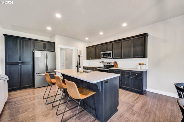 kitchen featuring appliances with stainless steel finishes, a kitchen island with sink, sink, and light wood-type flooring