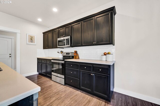 kitchen with tasteful backsplash, appliances with stainless steel finishes, light hardwood / wood-style floors, and dark brown cabinets