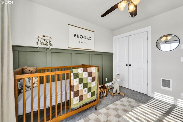 carpeted bedroom featuring ceiling fan, a closet, and a crib