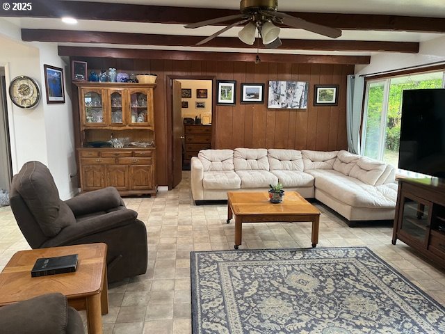 living room with wood walls, ceiling fan, and beam ceiling