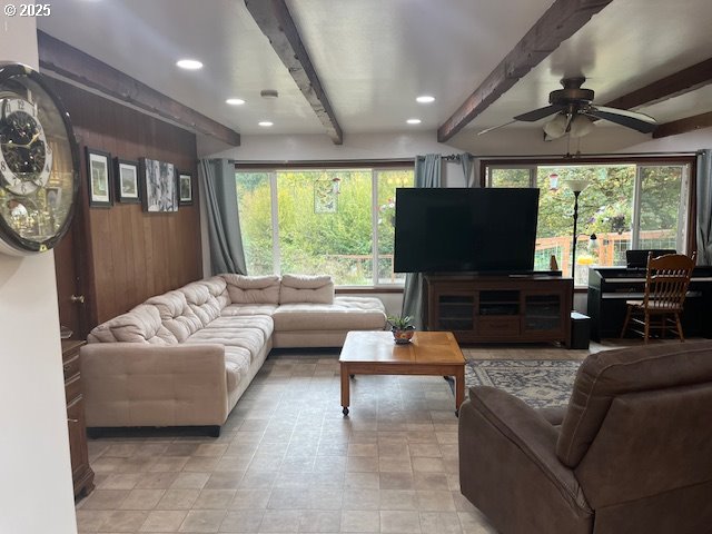 living room featuring wood walls, ceiling fan, and beamed ceiling