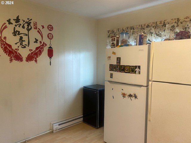 kitchen with white refrigerator, a baseboard heating unit, and light hardwood / wood-style floors