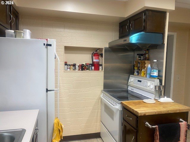 kitchen featuring butcher block counters, dark brown cabinets, sink, brick wall, and white appliances