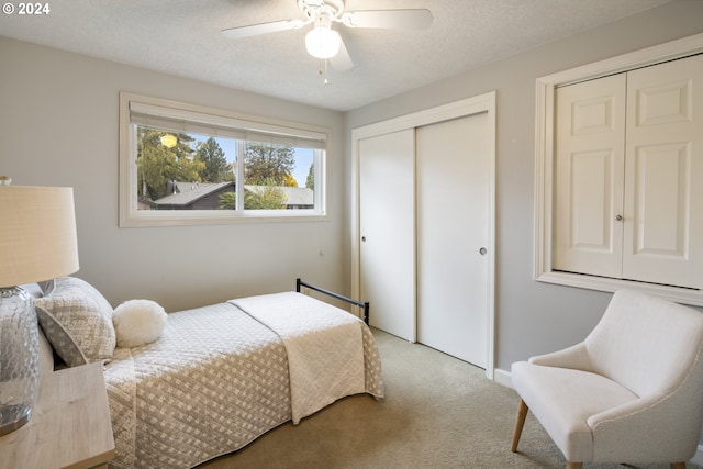 bedroom featuring light carpet, a textured ceiling, ceiling fan, and multiple closets