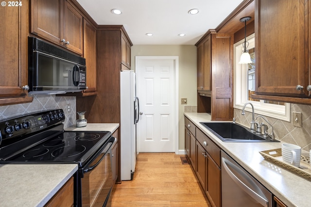 kitchen featuring black appliances, sink, decorative backsplash, light wood-type flooring, and decorative light fixtures