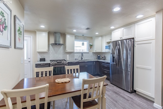 kitchen with white cabinetry, stainless steel appliances, backsplash, a sink, and wall chimney exhaust hood