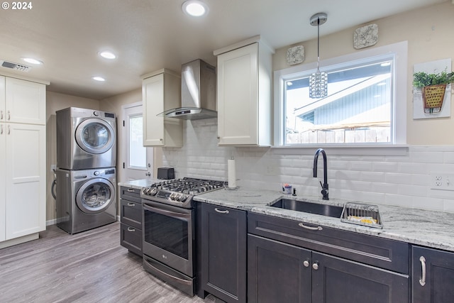 kitchen with a sink, stacked washer / dryer, gas stove, wall chimney range hood, and visible vents