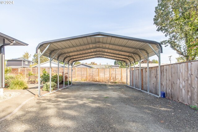 view of parking / parking lot featuring driveway, a detached carport, and fence