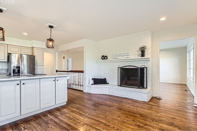 kitchen with stainless steel fridge, a brick fireplace, cooktop, dark wood-type flooring, and hanging light fixtures