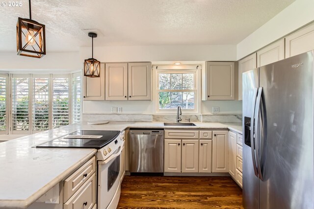 kitchen with sink, dark wood-type flooring, pendant lighting, a textured ceiling, and appliances with stainless steel finishes