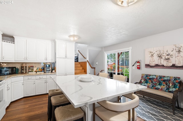 kitchen with white cabinets, dark hardwood / wood-style floors, light stone countertops, and a breakfast bar area