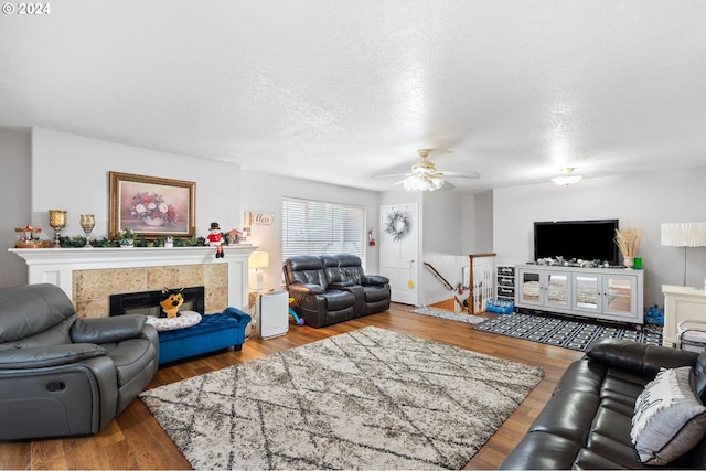 living room with hardwood / wood-style flooring, a textured ceiling, a tile fireplace, and ceiling fan