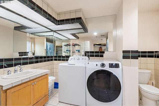 laundry room featuring light tile patterned flooring, tile walls, washing machine and dryer, and sink