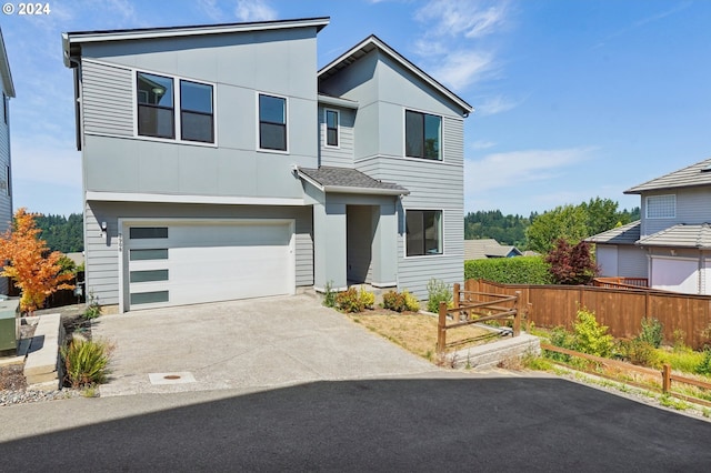 contemporary home featuring driveway, an attached garage, and fence