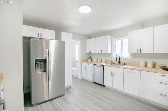 kitchen featuring white cabinets, appliances with stainless steel finishes, light countertops, and a sink