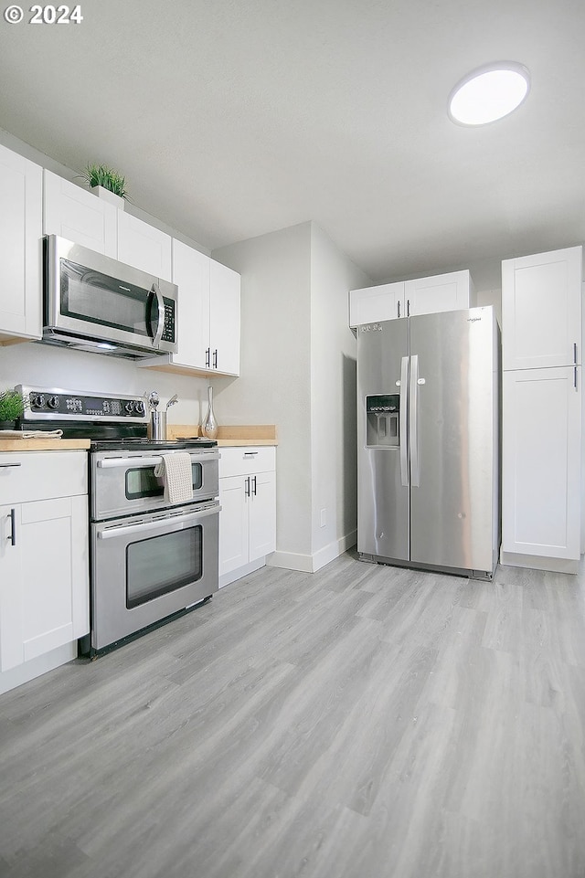 kitchen featuring baseboards, white cabinets, wooden counters, appliances with stainless steel finishes, and light wood finished floors