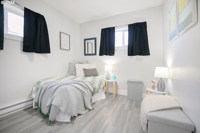 bedroom with baseboards, a baseboard radiator, and light wood-style floors