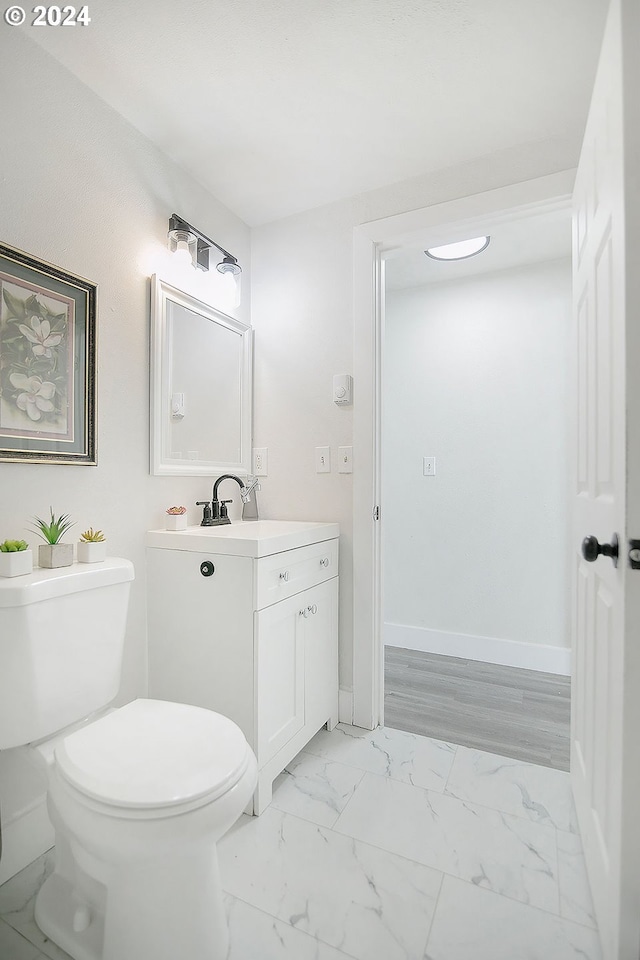 half bathroom featuring marble finish floor, baseboards, vanity, and toilet