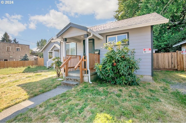 bungalow-style house with a shingled roof, a front yard, and fence