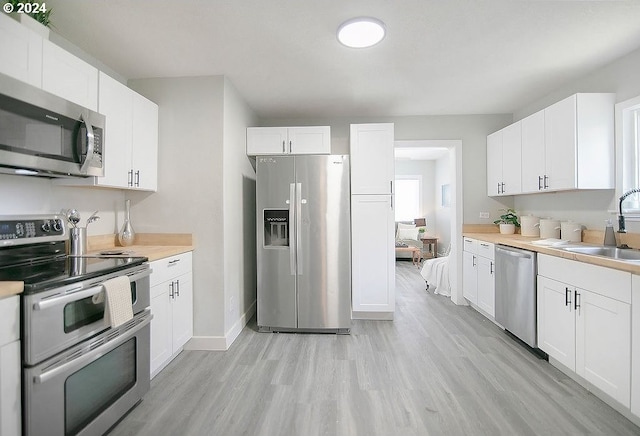 kitchen with light wood-style flooring, stainless steel appliances, light countertops, white cabinetry, and a sink