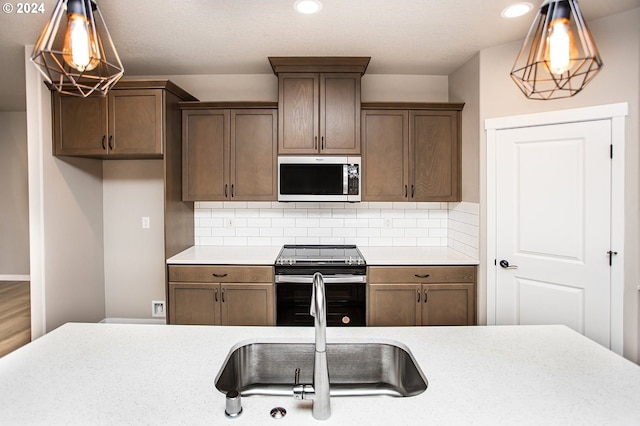 kitchen featuring sink, backsplash, decorative light fixtures, appliances with stainless steel finishes, and hardwood / wood-style flooring