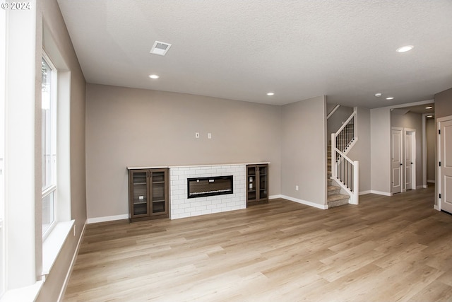 unfurnished living room with a fireplace, a textured ceiling, and light wood-type flooring