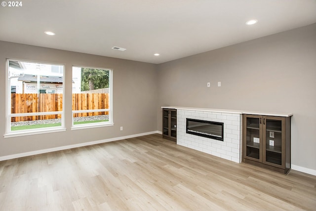 unfurnished living room with light wood-type flooring and a brick fireplace