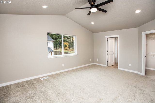 unfurnished bedroom featuring ceiling fan, lofted ceiling, a walk in closet, light carpet, and a closet