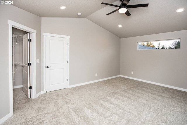 unfurnished bedroom featuring lofted ceiling, light carpet, a walk in closet, ceiling fan, and a closet