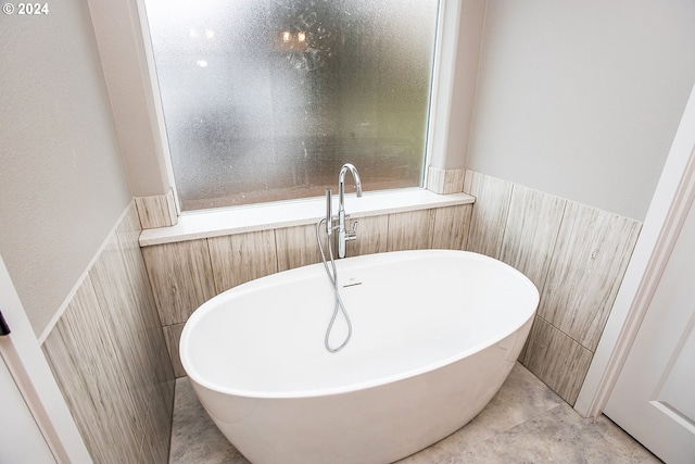 bathroom featuring tile patterned flooring, a bath, and tile walls