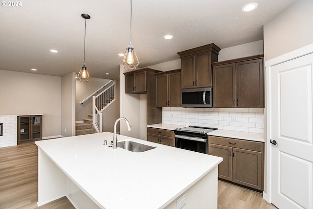 kitchen with pendant lighting, sink, range with electric stovetop, an island with sink, and light hardwood / wood-style floors