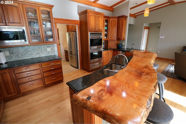 kitchen featuring dark stone countertops, appliances with stainless steel finishes, sink, and vaulted ceiling with beams