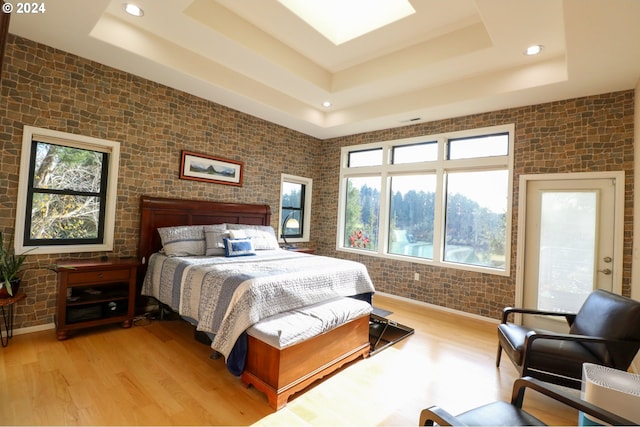 bedroom featuring brick wall, a tray ceiling, and light hardwood / wood-style flooring