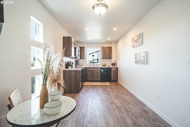 kitchen featuring wood finished floors, light countertops, baseboards, stainless steel microwave, and black dishwasher