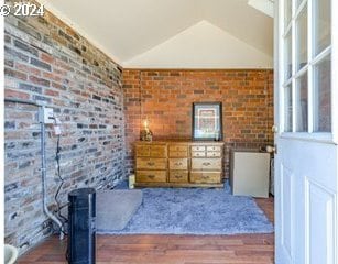 living area featuring dark hardwood / wood-style floors, vaulted ceiling, and brick wall