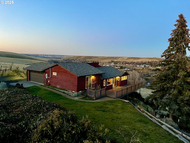 back house at dusk featuring a garage, a deck, and a lawn