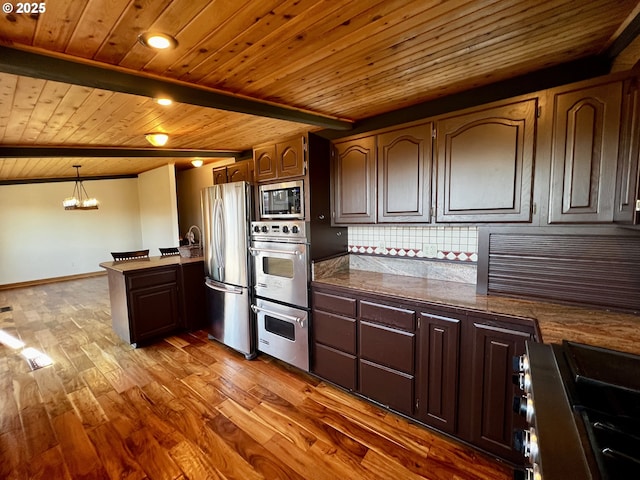 kitchen featuring dark countertops, backsplash, beam ceiling, wood finished floors, and stainless steel appliances