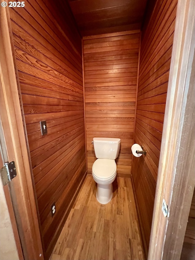 bathroom featuring toilet, wood finished floors, and wooden walls