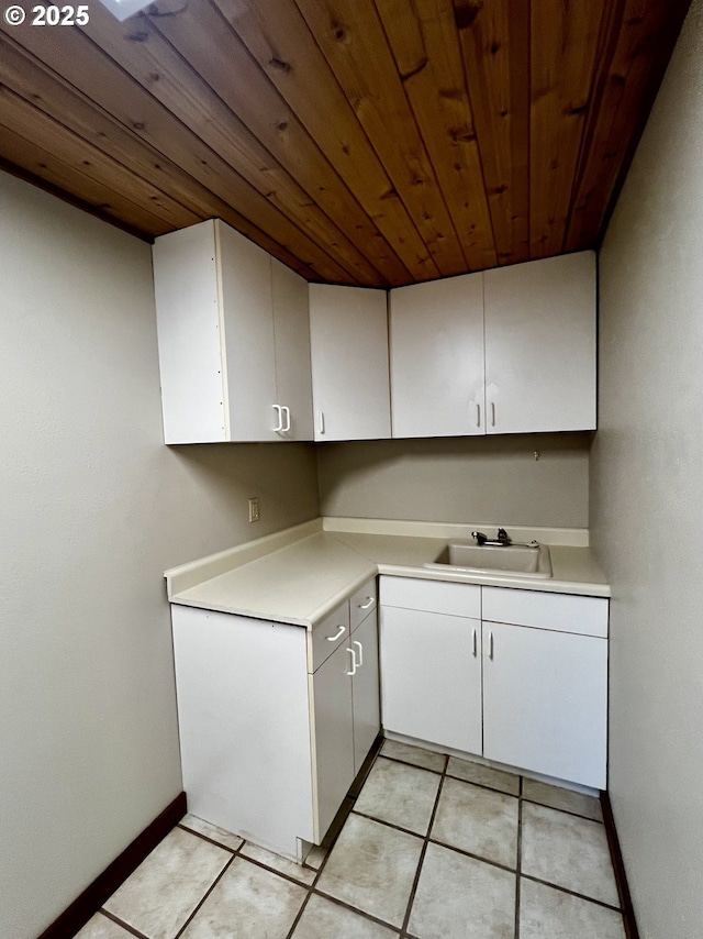 kitchen with a sink, white cabinetry, wooden ceiling, light countertops, and baseboards