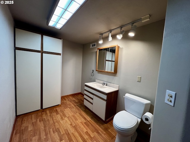 half bathroom featuring visible vents, toilet, rail lighting, wood finished floors, and vanity