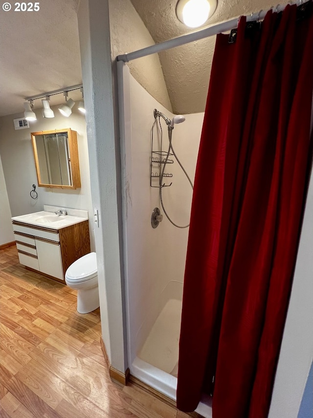 bathroom featuring visible vents, toilet, a stall shower, a textured ceiling, and wood finished floors