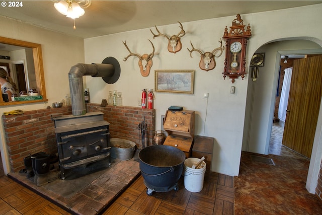 interior space with dark parquet flooring, ceiling fan, and a wood stove