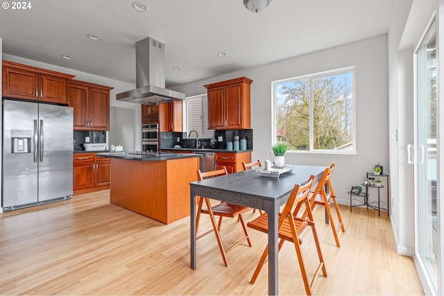 kitchen featuring a center island, backsplash, light wood-type flooring, island exhaust hood, and stainless steel appliances