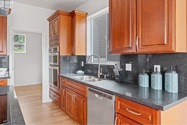 kitchen featuring sink, dark stone countertops, decorative backsplash, appliances with stainless steel finishes, and light wood-type flooring