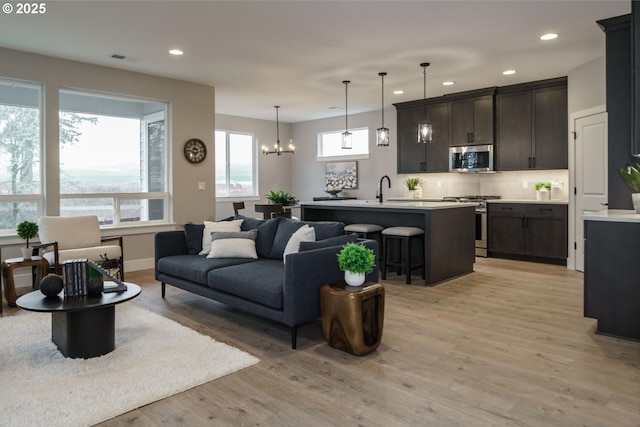 living room with a healthy amount of sunlight, light wood-type flooring, a notable chandelier, and sink