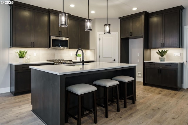 kitchen featuring decorative light fixtures, sink, light hardwood / wood-style floors, and an island with sink