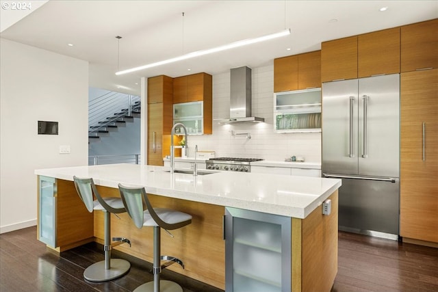 kitchen featuring backsplash, decorative light fixtures, dark hardwood / wood-style floors, stainless steel built in fridge, and wall chimney range hood