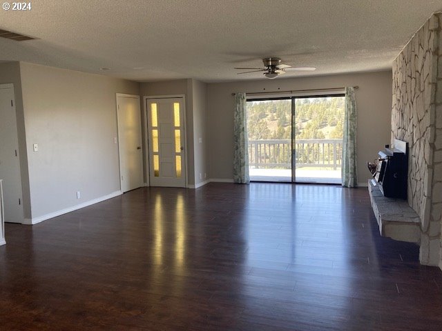 unfurnished living room with ceiling fan, a fireplace, dark hardwood / wood-style flooring, and a textured ceiling